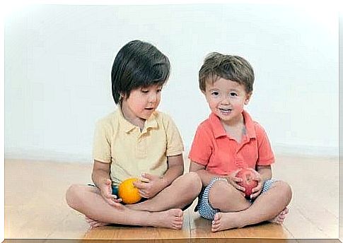 Siblings sitting on the floor with a fruit in their hand and getting along well.